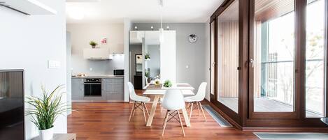 Una cocina moderna con armarios blancos, un comedor con una mesa y sillas blancas, y un amplio ventanal corredero al exterior.