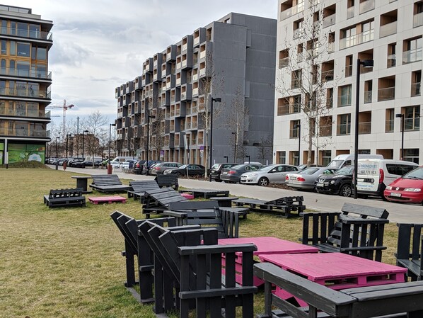 A modern apartment building with multiple floors and balconies, a parking area with several cars, and outdoor seating with tables and benches. - Apartment4you Select Kolejowa (Warsaw)