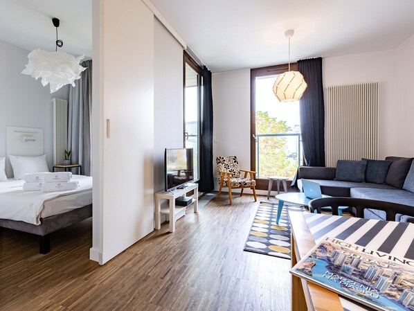 A modern hotel room with a bed, TV, seating area, and a view of the outdoors.