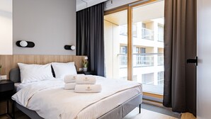 Een moderne hotelkamer met een groot bed, een nachtkastje met een lamp, een plant in pot en uitzicht op het gebouw.