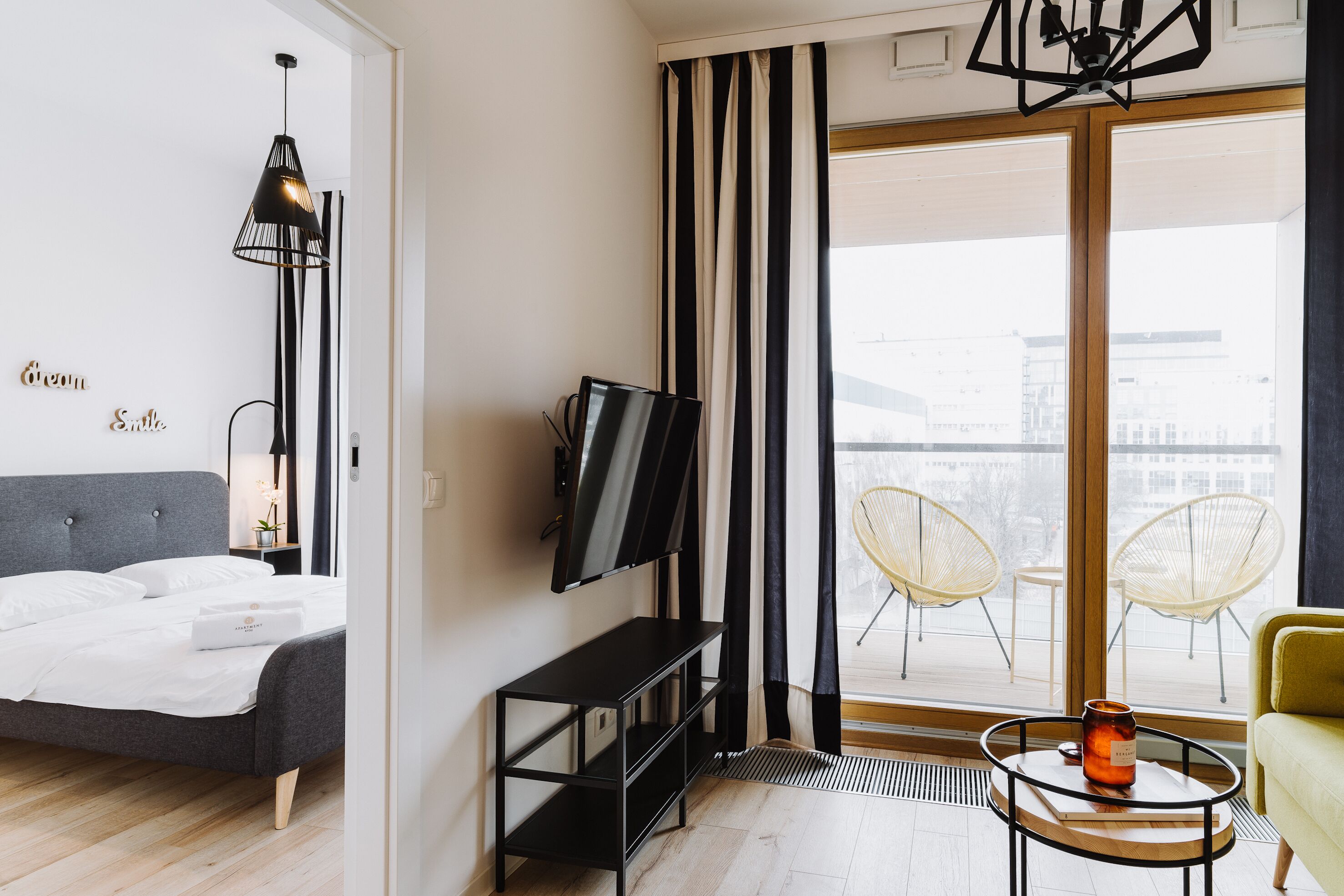 Una habitación de hotel moderna con cama, televisor, una mesita con vela y balcón con sillas.