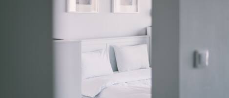 Een wit bed met hoofdeinde, een gedeeltelijk open deur en twee ingelijste foto's aan de muur.
