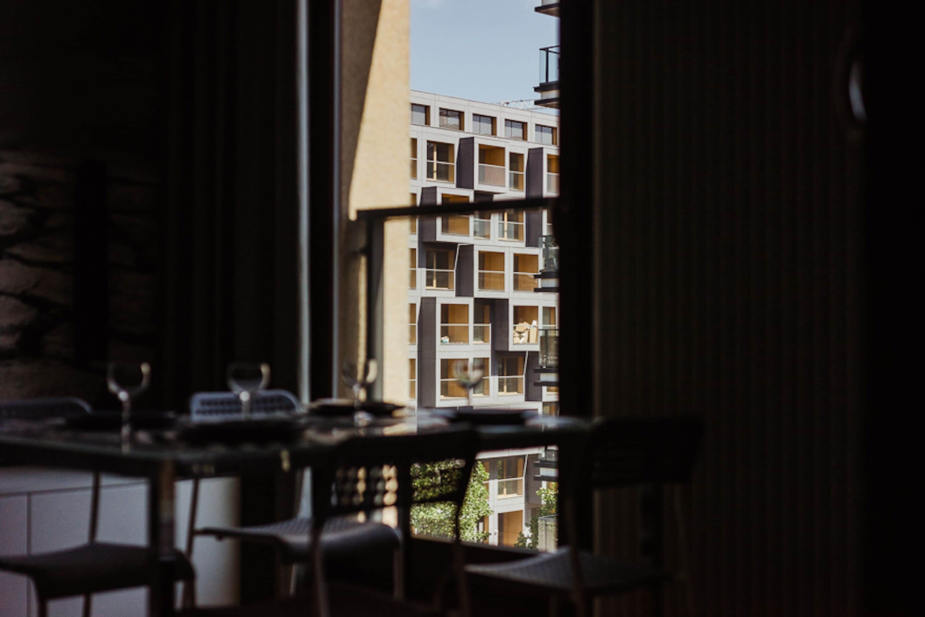 A view from a window with a table and chairs, overlooking a modern building with balconies.