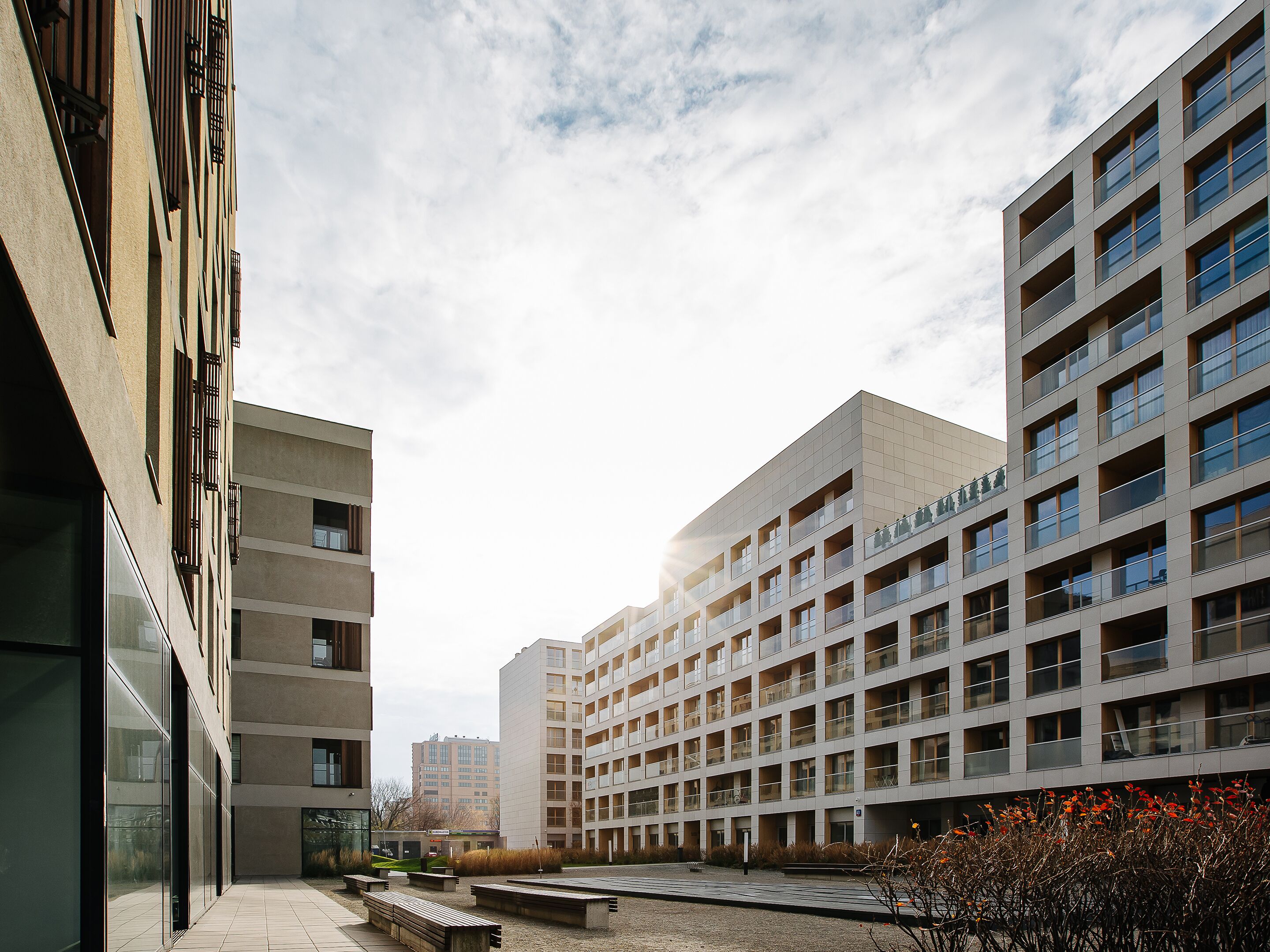 Un edificio moderno con varios pisos, grandes ventanales y un patio con bancos.