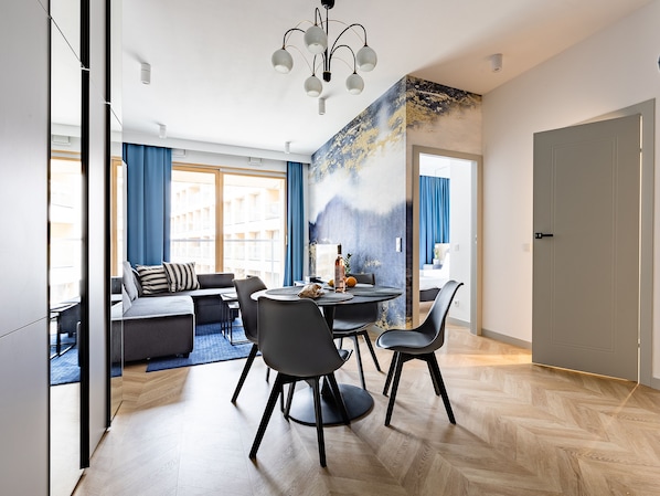 Una habitación de hotel moderna con zona de comedor, sofá y vistas a la ciudad.