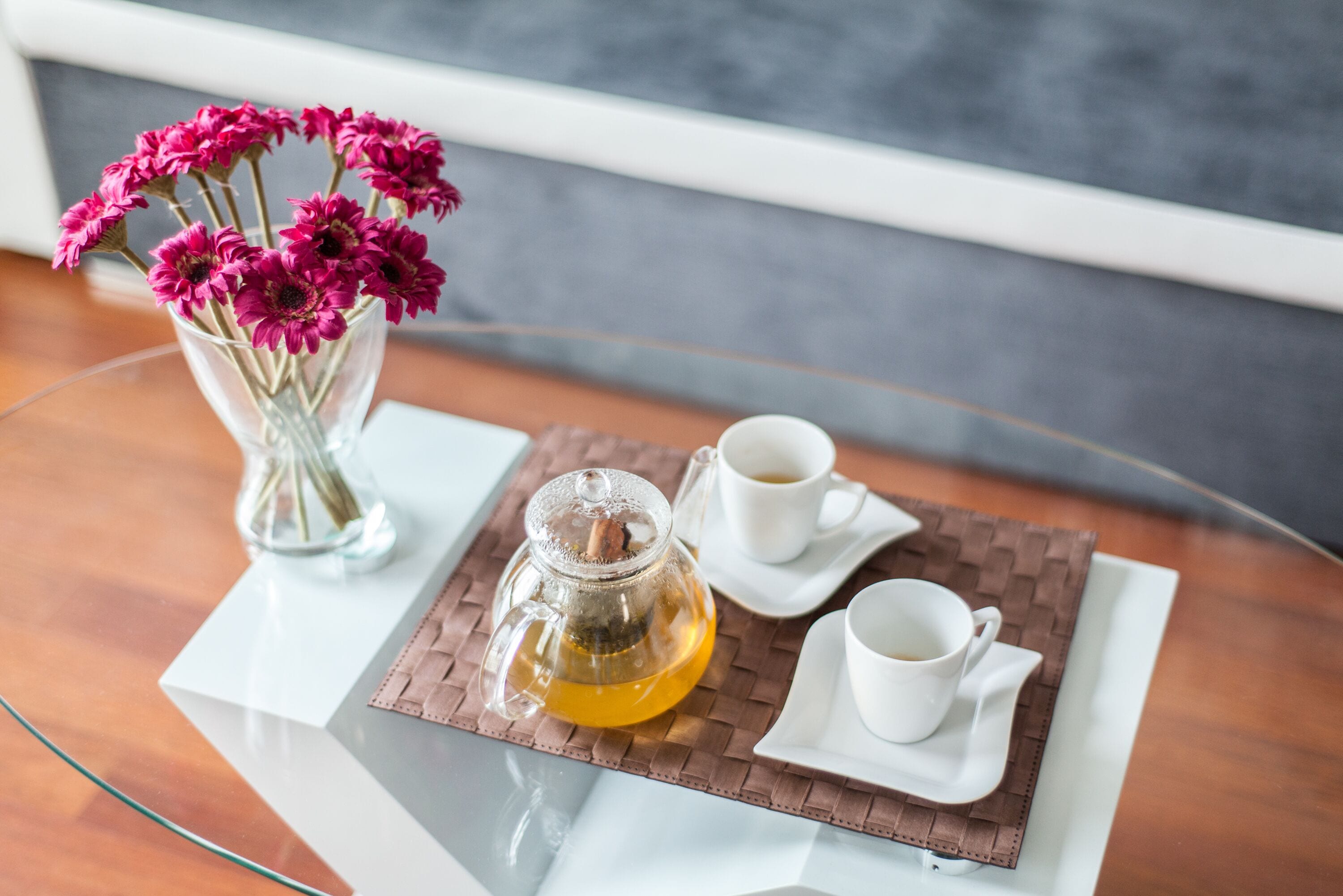 A clear glass table with a white pitcher, two white cups, and a woven placemat.