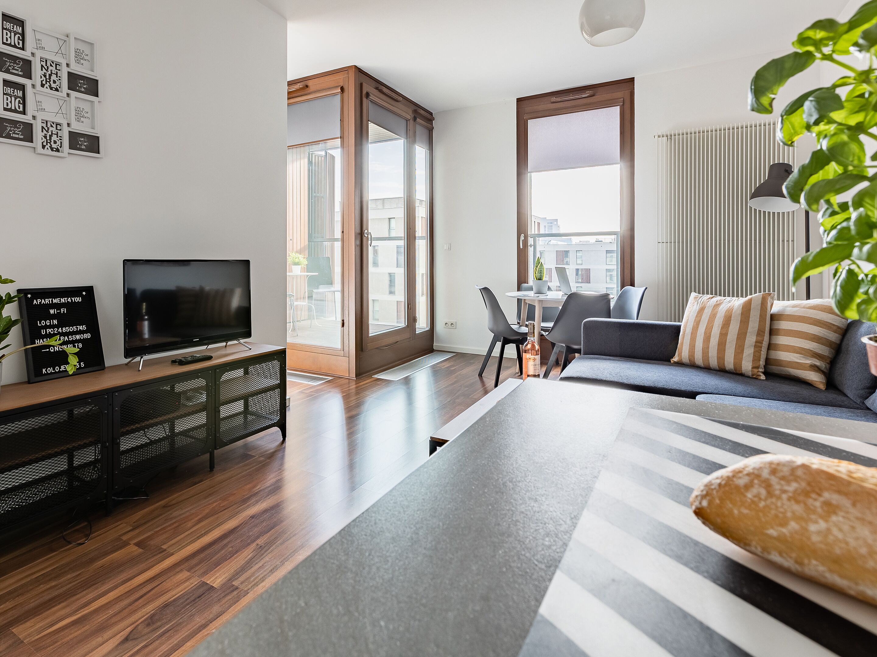 A modern living room with a flat-screen TV, a coffee table, a sofa, and a dining area with chairs.