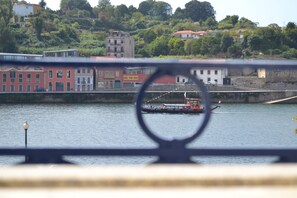 A river with a boat, buildings in the background, and a bridge railing in the foreground. - Happy Porto Hostel & Apartments (Porto)
