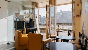 Interior de restaurante com cadeiras amarelas, uma mesa preta e uma parede de vidro que oferece vista para a rua.
