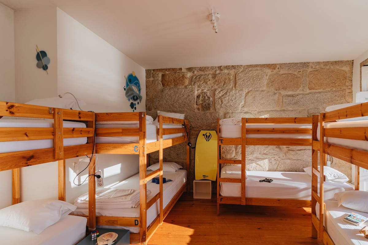 Ein Schlafraum mit Etagenbetten aus Holz, einer Steinwand und einem Surfbrett an der Wand.