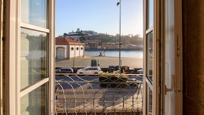 Vista da janela sobre uma área à beira-mar com uma ponte, carros estacionados e edifícios ao fundo.
