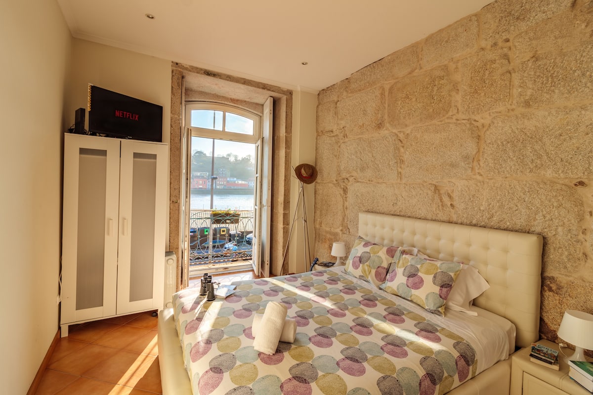 Ein Schlafzimmer mit Bett, Kleiderschrank, Fernseher und Blick ins Freie.