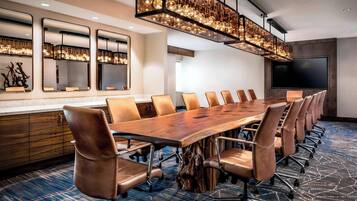 A conference room with a long wooden table, leather chairs, a large TV, and a unique hanging light fixture.