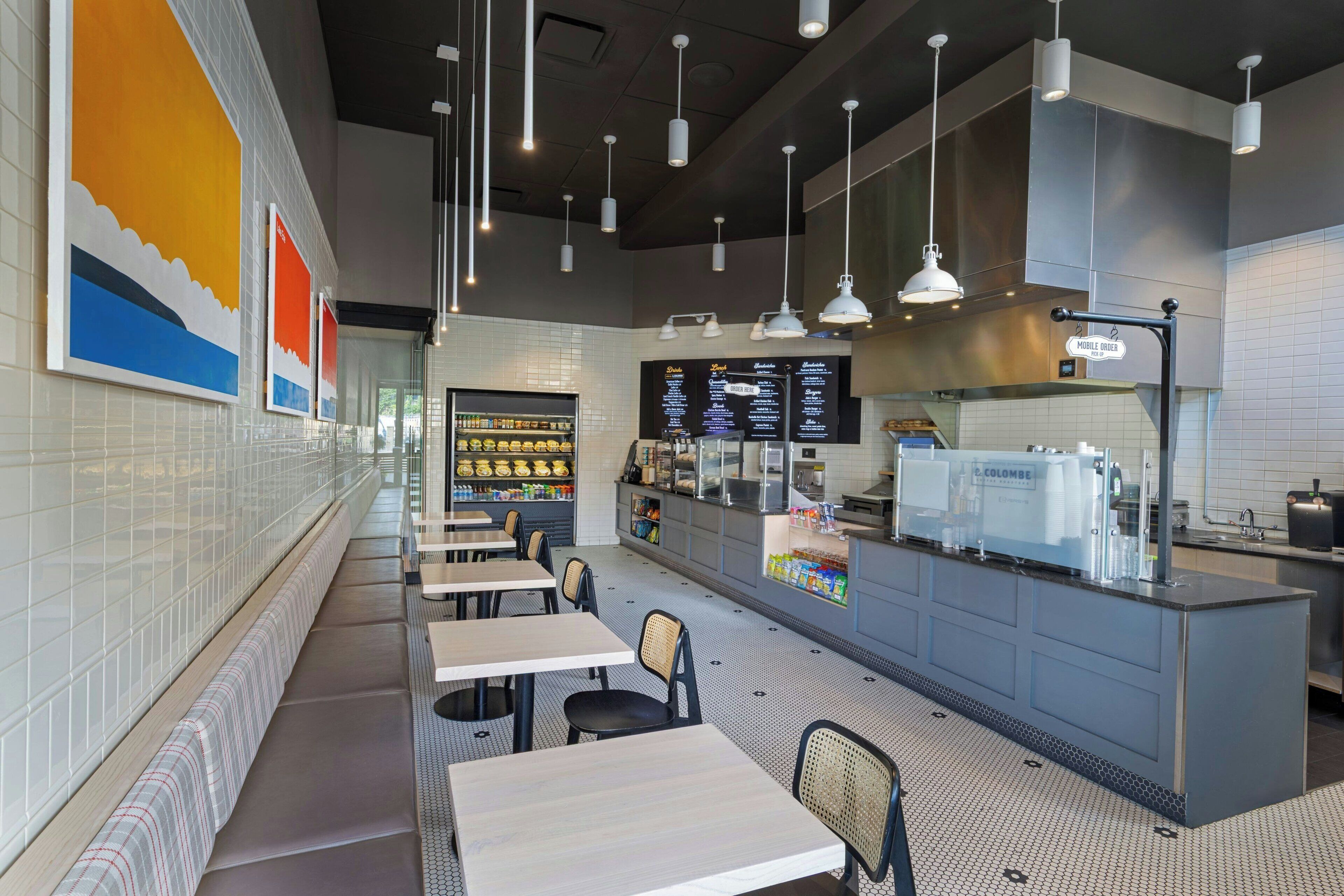 A modern cafe interior with long tables, hanging pendant lights, and a menu board.