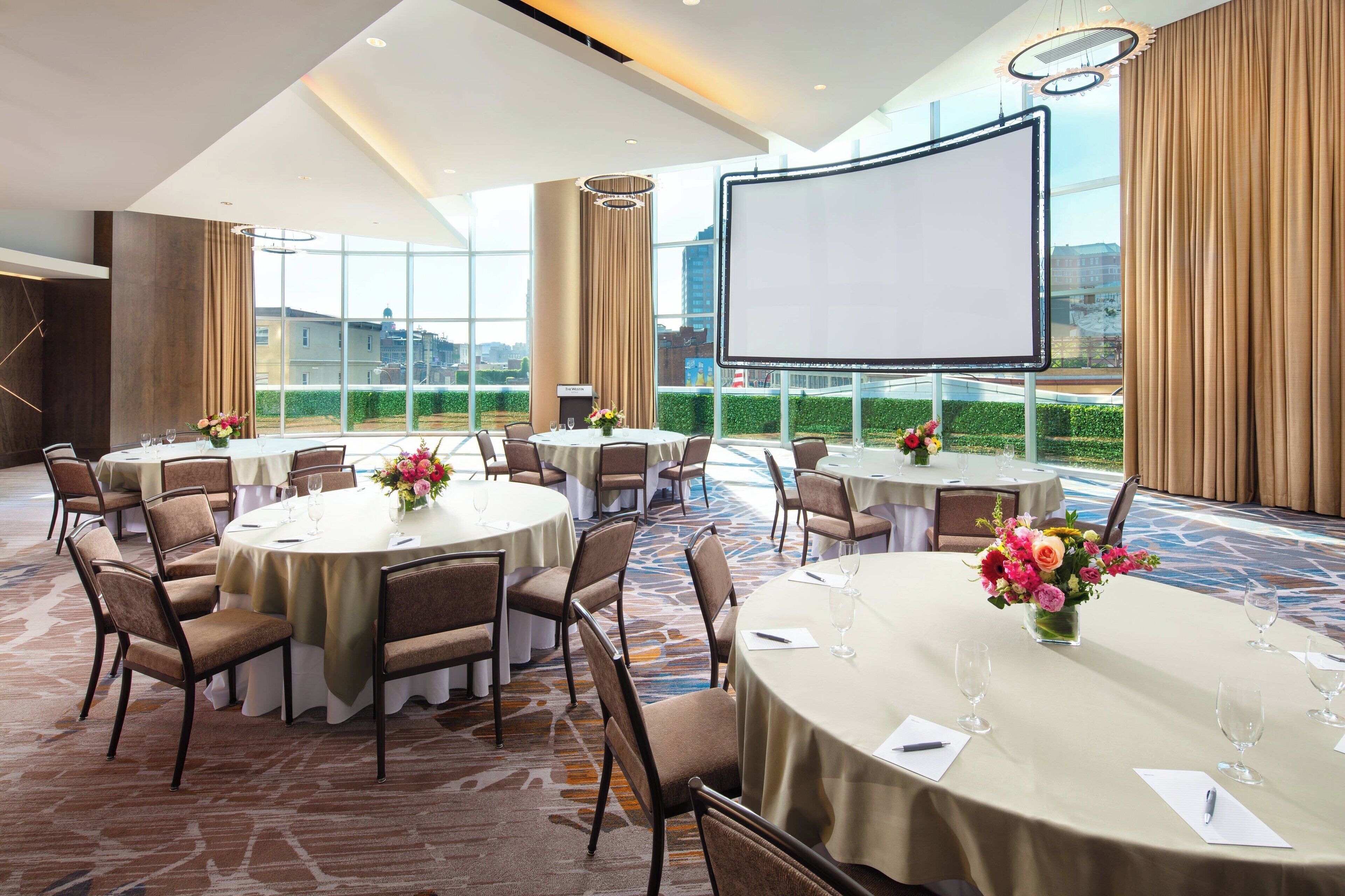 A conference room with multiple round tables, chairs, and a large screen.
