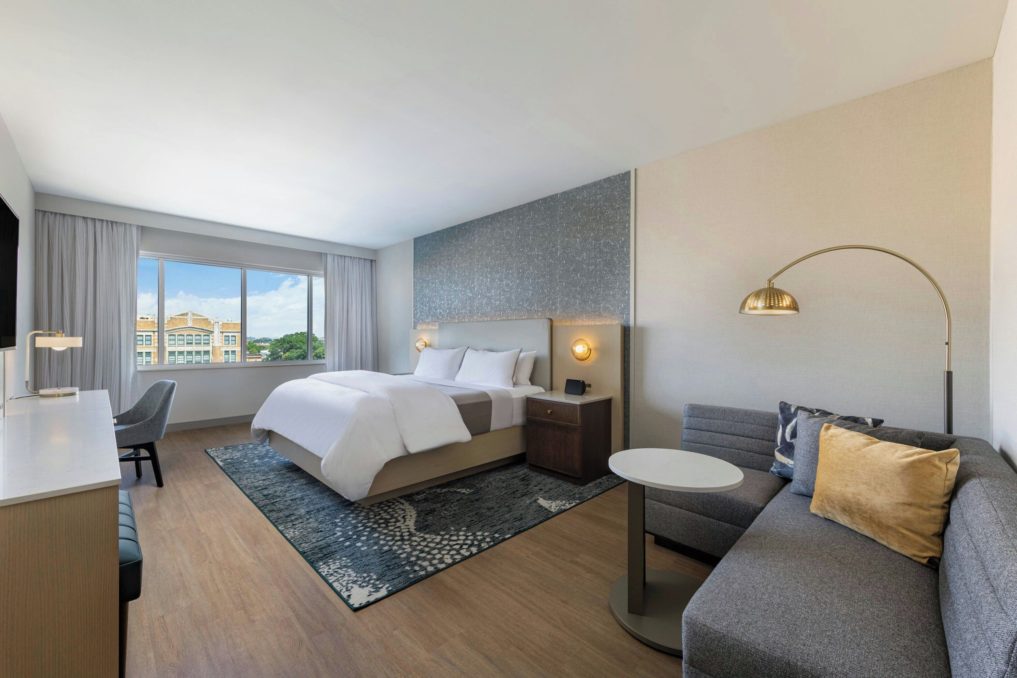 Una habitación de hotel moderna con una cama grande, un escritorio, un sofá y vistas de la ciudad.