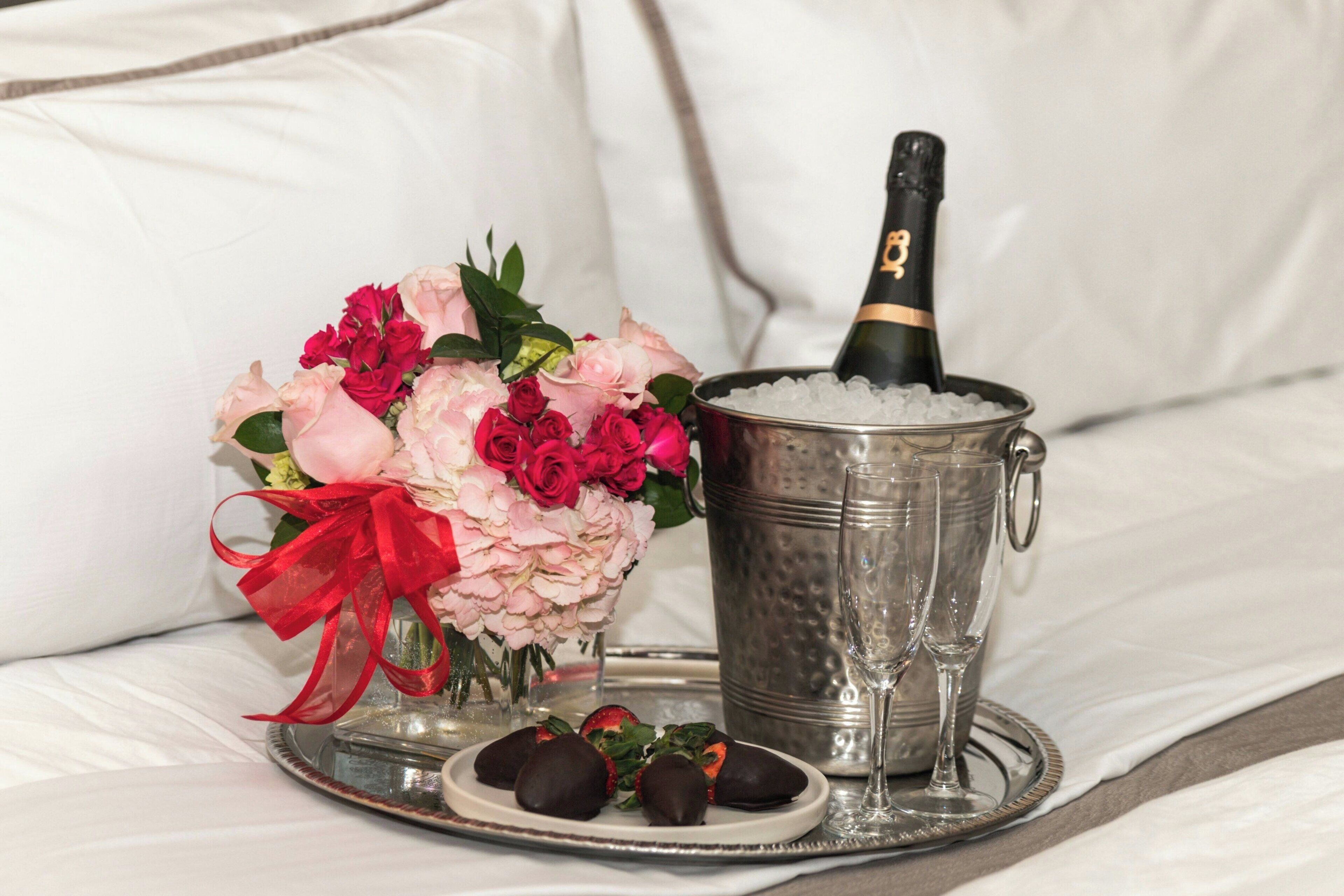 Uma cama com um balde de metal contendo uma garrafa de champanhe, uma taça e um prato com morangos cobertos de chocolate.
