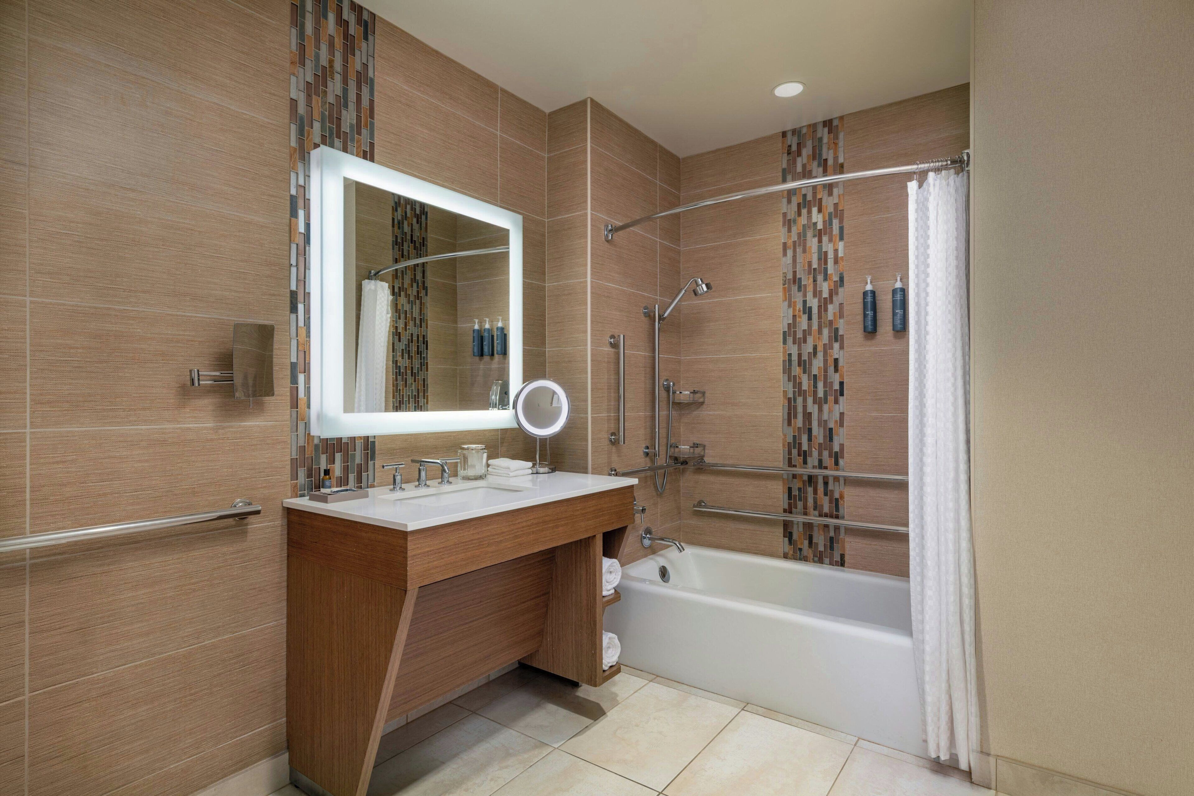 Un bagno moderno con un mobile lavabo in legno, uno specchio grande, una vasca e uno spazio doccia.