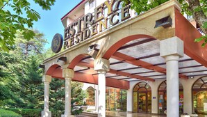 Entrada de un hotel con un porche cubierto, columnas y un letrero que dice 'Hotel Residence'.