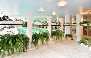 A spacious indoor area with a pool, white columns, and various potted plants. - Estreya Palace & Residence (Varna)