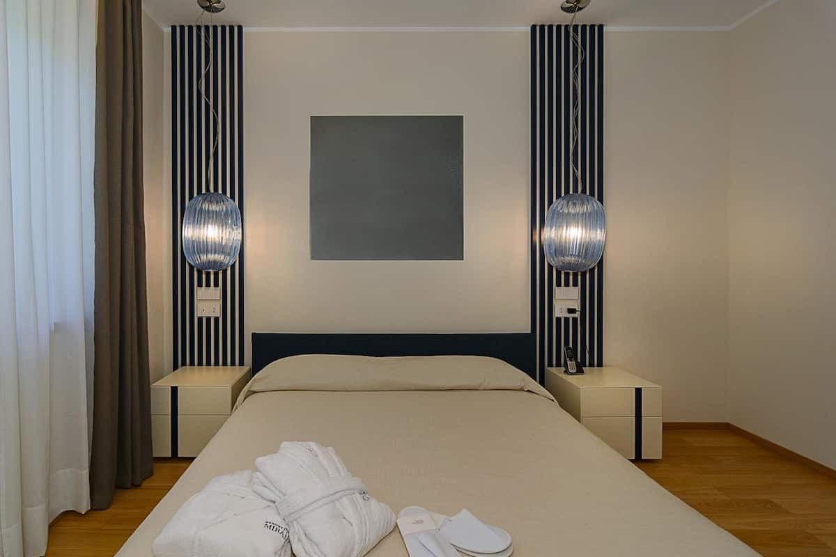 A hotel room with a bed, bedside tables, a robe, slippers, and a large abstract painting on the wall.