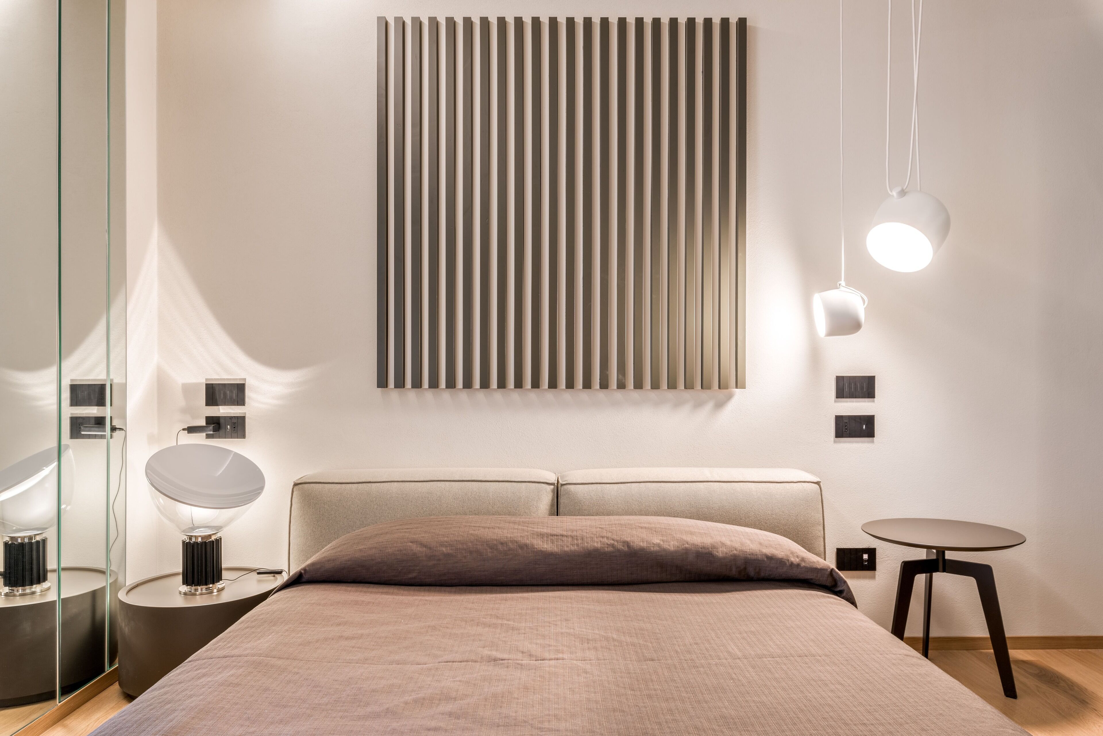 A modern bedroom with a large bed, bedside tables, a wall-mounted light fixture, and a mirror.