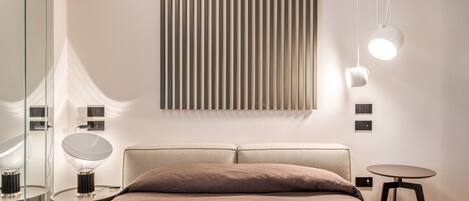 A modern bedroom with a large bed, bedside tables, a wall-mounted light fixture, and a mirror.