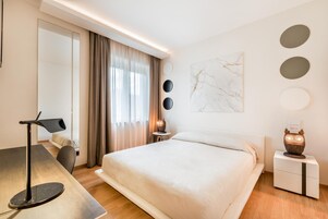 Una habitación de hotel moderna con una cama grande, un escritorio con lámpara, una mesita con lámpara y una mesita de noche con un búho decorativo.