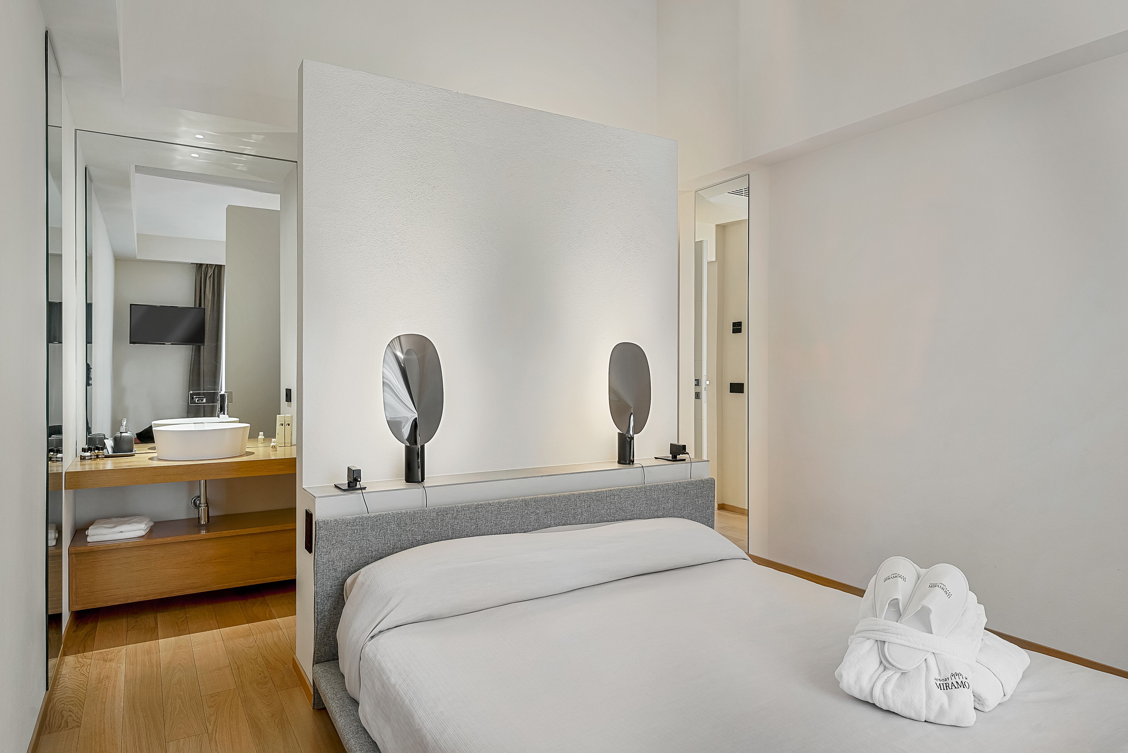 A modern hotel room with a large bed, a vanity with a mirror, and a flat-screen TV.