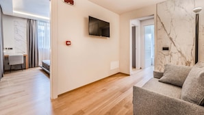 A modern living room with a flat-screen TV mounted on the wall, a grey sofa, and a wooden floor. - Resort Miramonti (Forte dei Marmi)