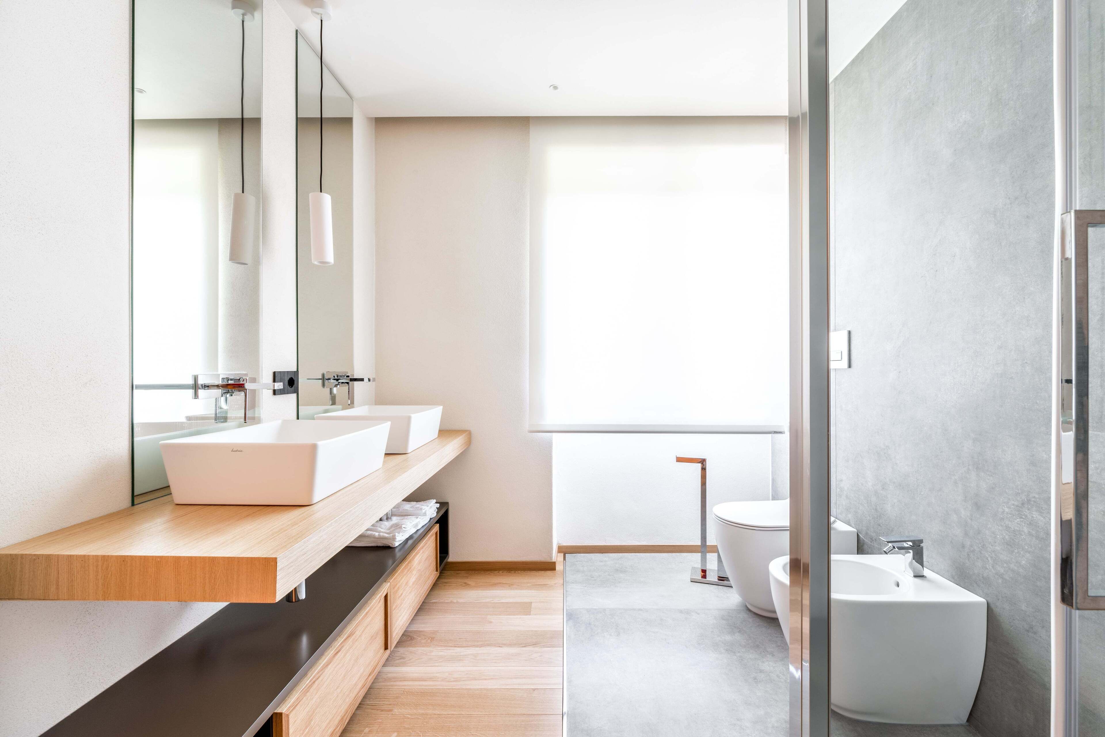A modern bathroom with a large mirror, two sinks, a bidet, and a shower area.