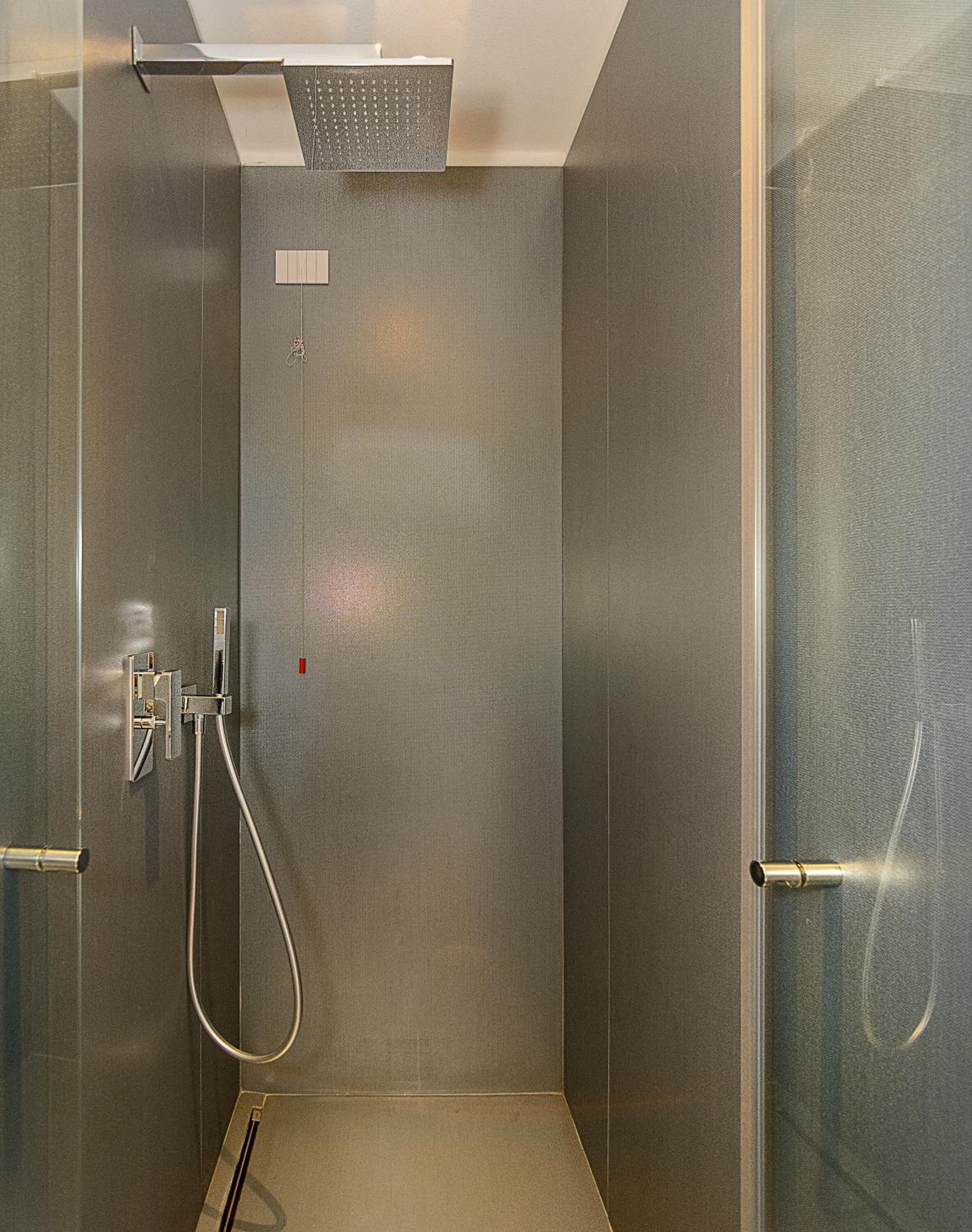 A modern shower with a handheld showerhead and a fixed showerhead, a control panel, and a glass door.