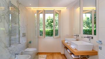 Une salle de bain moderne avec un mur en marbre, une grande fenêtre, un lavabo blanc et un meuble-lavabo en bois.