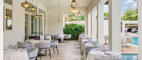 A restaurant with round tables, chairs, and hanging pendant lights.