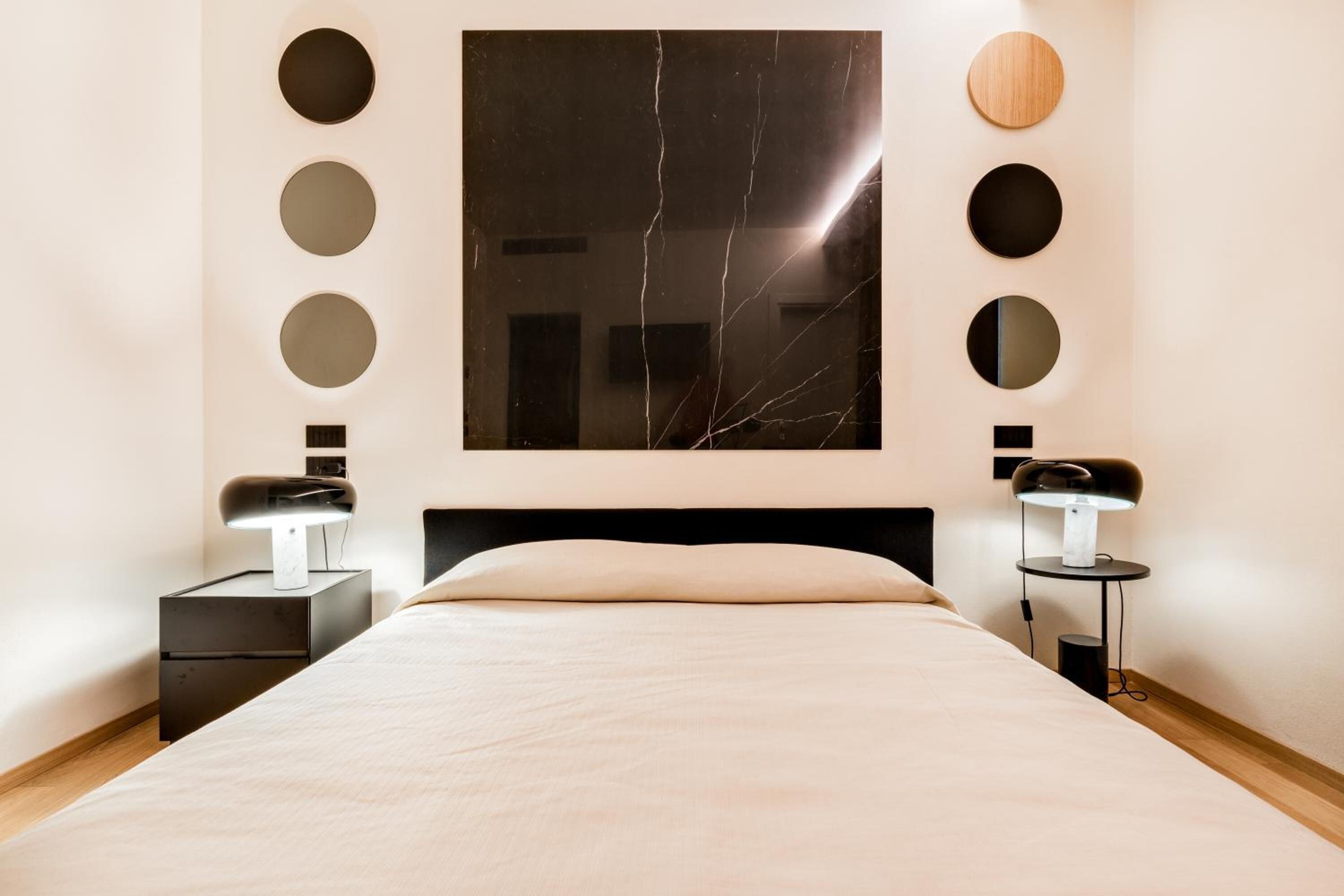 Un dormitorio moderno con una cama grande, dos mesitas de noche, un espejo montado en la pared y un cuadro abstracto de gran tamaño.