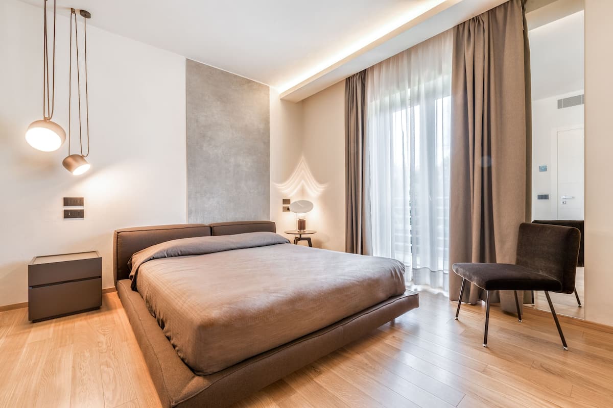 A modern bedroom with a large bed, bedside tables, a chair, and a window with curtains.