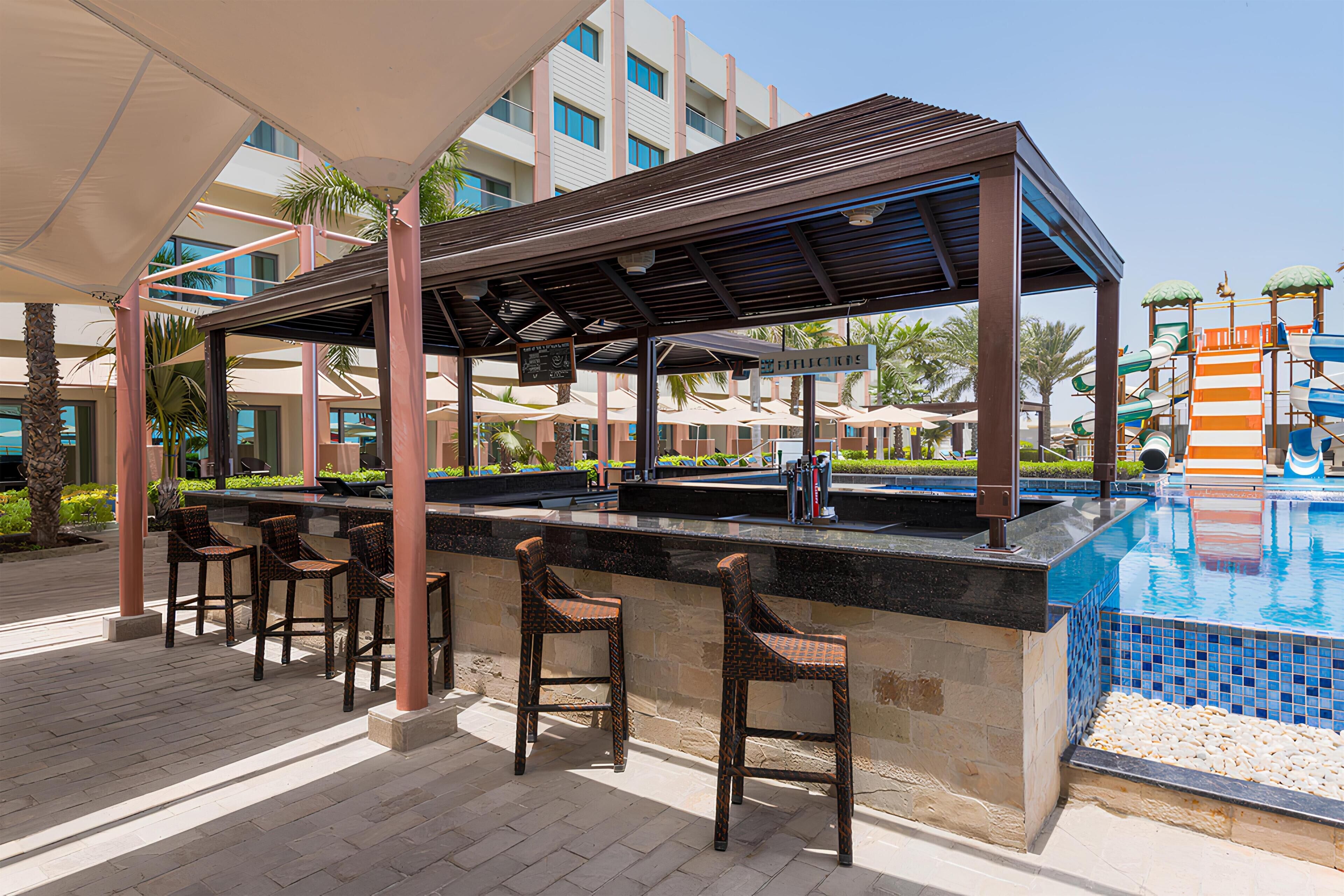 A poolside bar area with a covered seating area, a pool, and a water slide.
