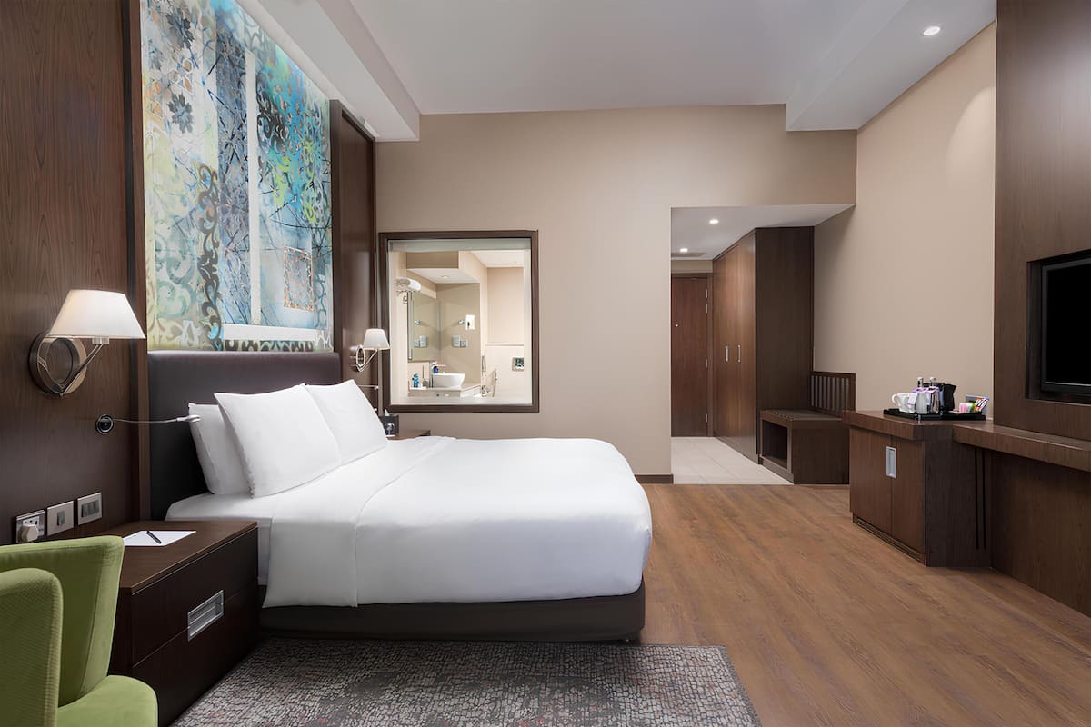 Una habitación de hotel con una cama grande, un escritorio con lámpara, una televisión y un cuadro en la pared.