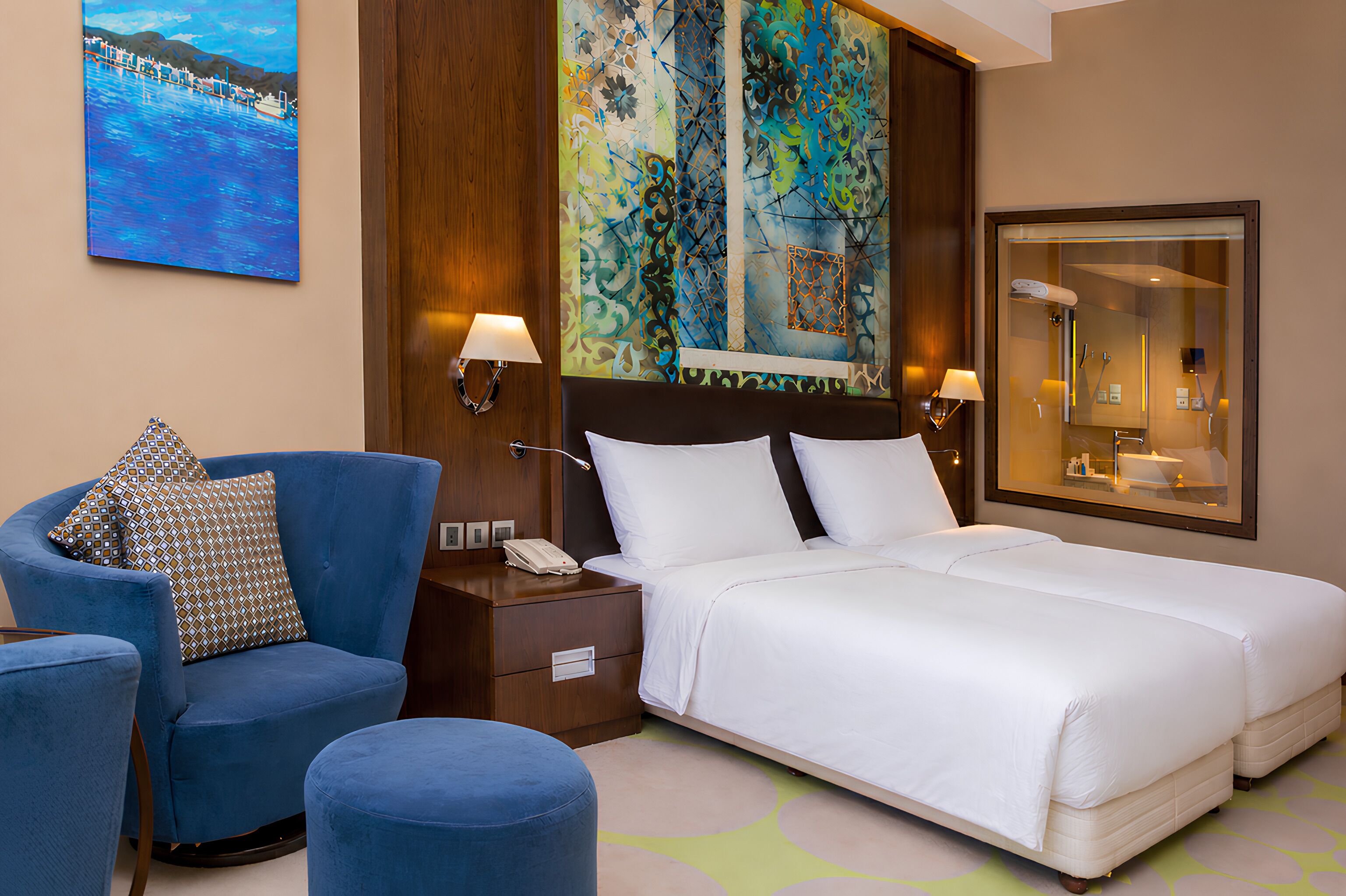 Una habitación de hotel con cama, una silla, una mesita de noche, una lámpara y un cuadro en la pared.