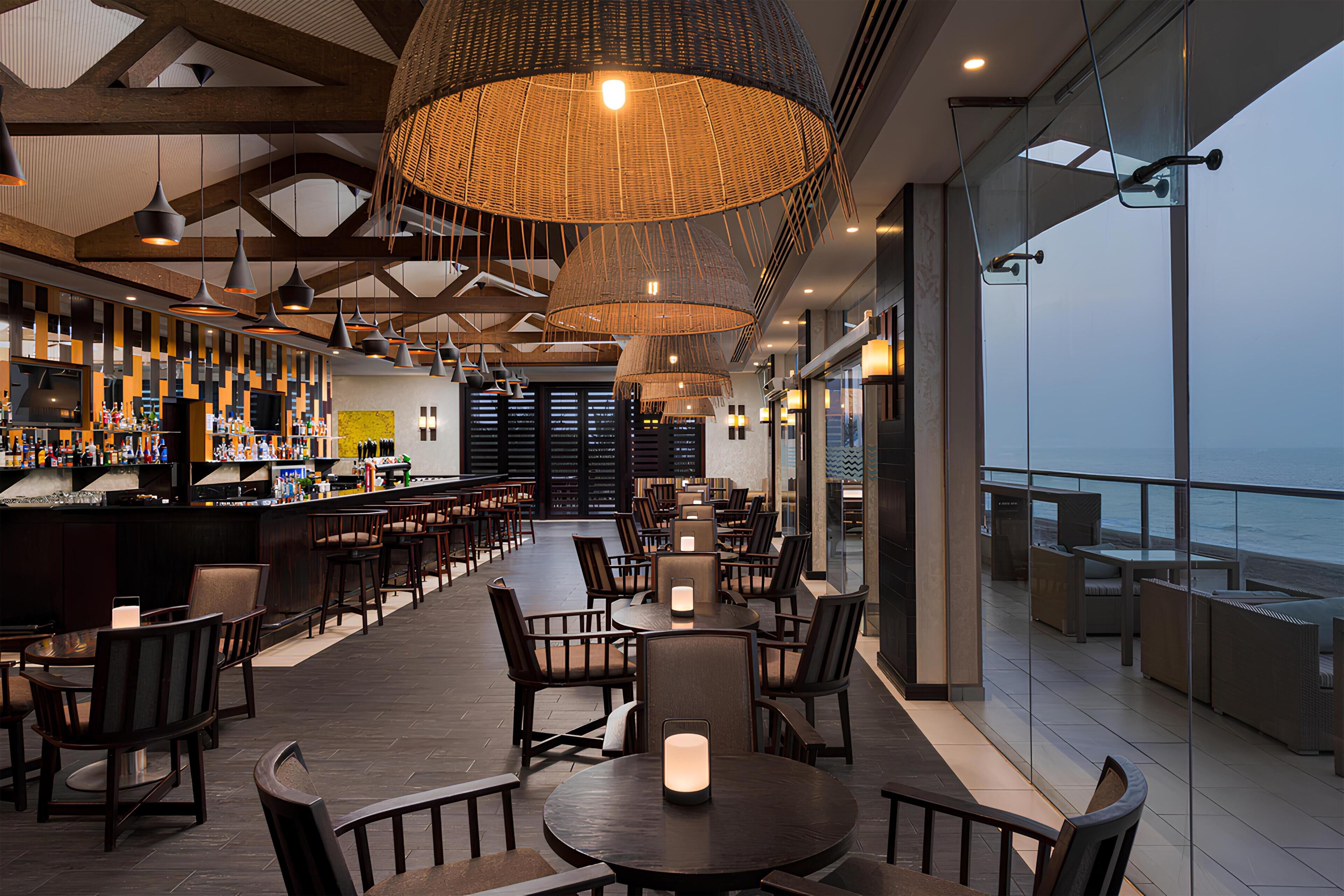 A modern bar area with seating, large pendant lights, and a view of the ocean.
