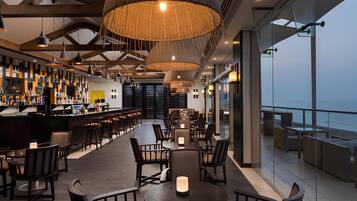 A modern bar area with seating, large pendant lights, and a view of the ocean.