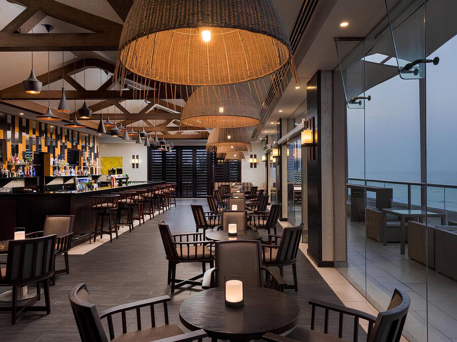Zona bar moderna con posti a sedere, grandi lampade a sospensione e vista sull'oceano.
