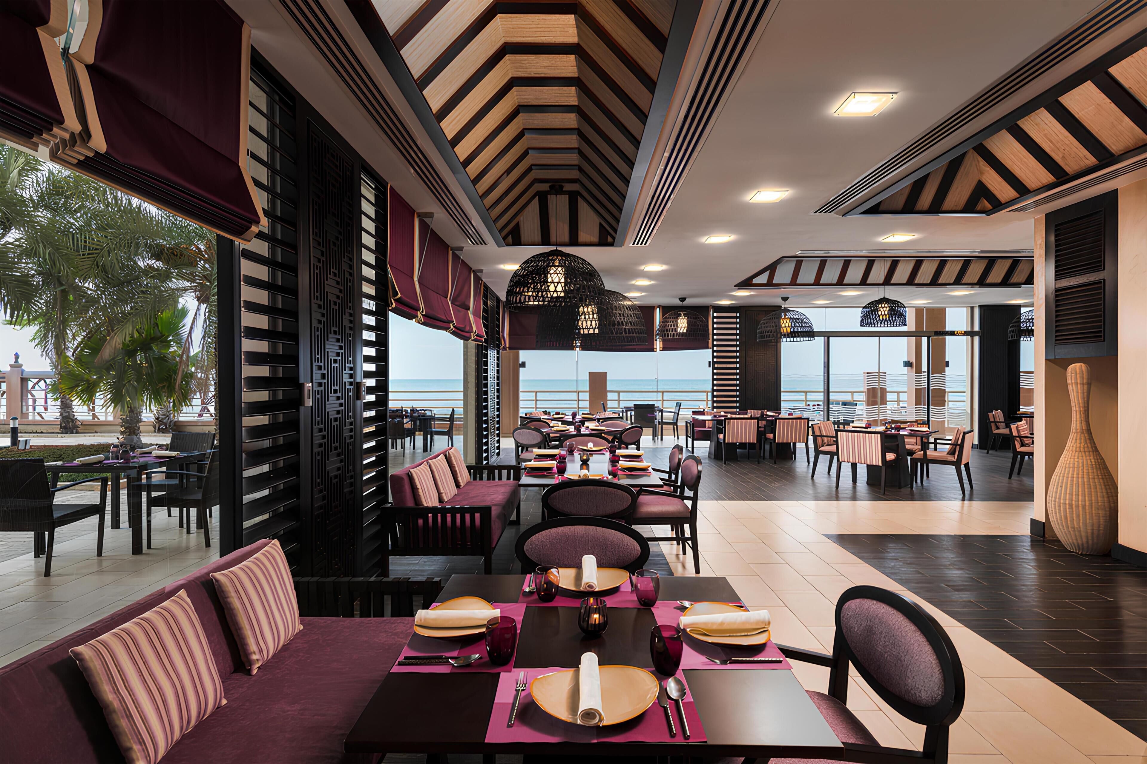 A restaurant with tables set for dining, a view of the sea, and a modern interior design.