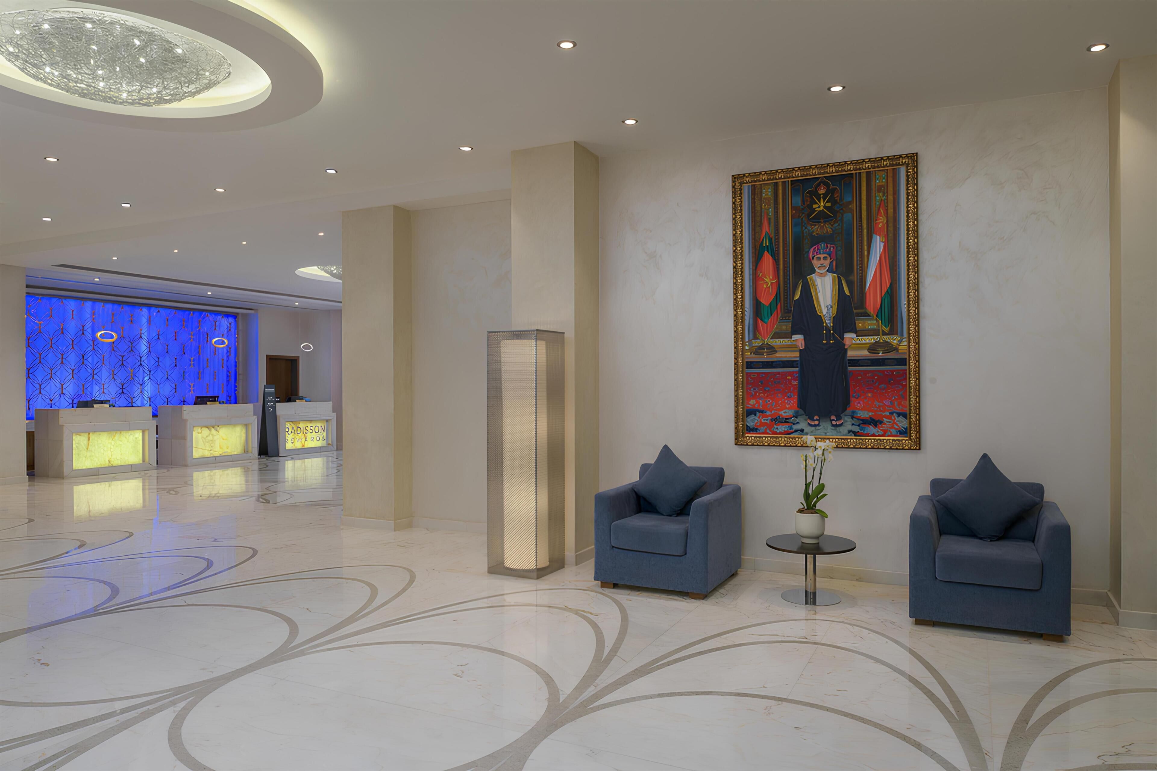 A lobby with a reception desk, two armchairs, a tall floor lamp, and a large framed painting.
