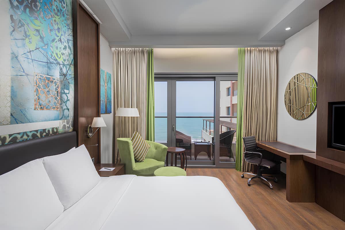 Habitación de hotel con cama, escritorio, silla, mesita y vista al océano.