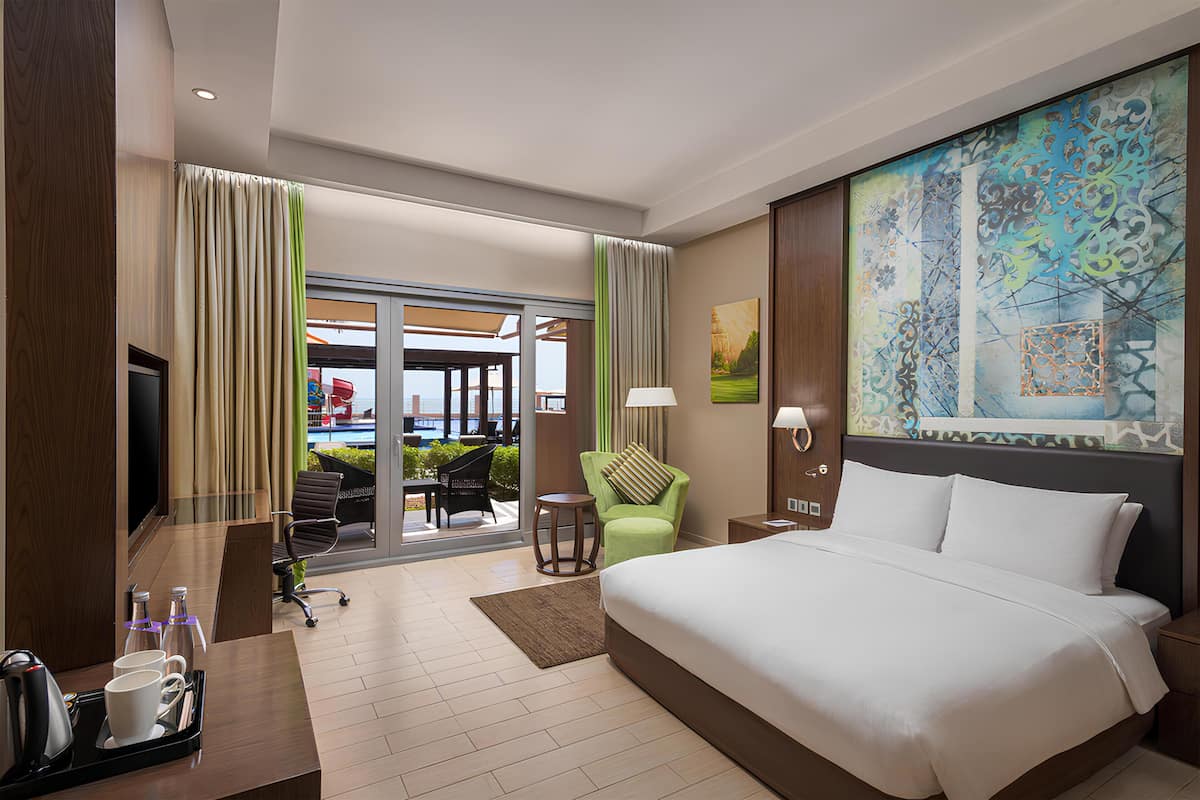 Habitación de hotel con una cama grande, un escritorio con cafetera, una silla y vistas al exterior.