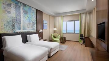 A hotel room with two beds, a TV, a desk, and a window with a view.