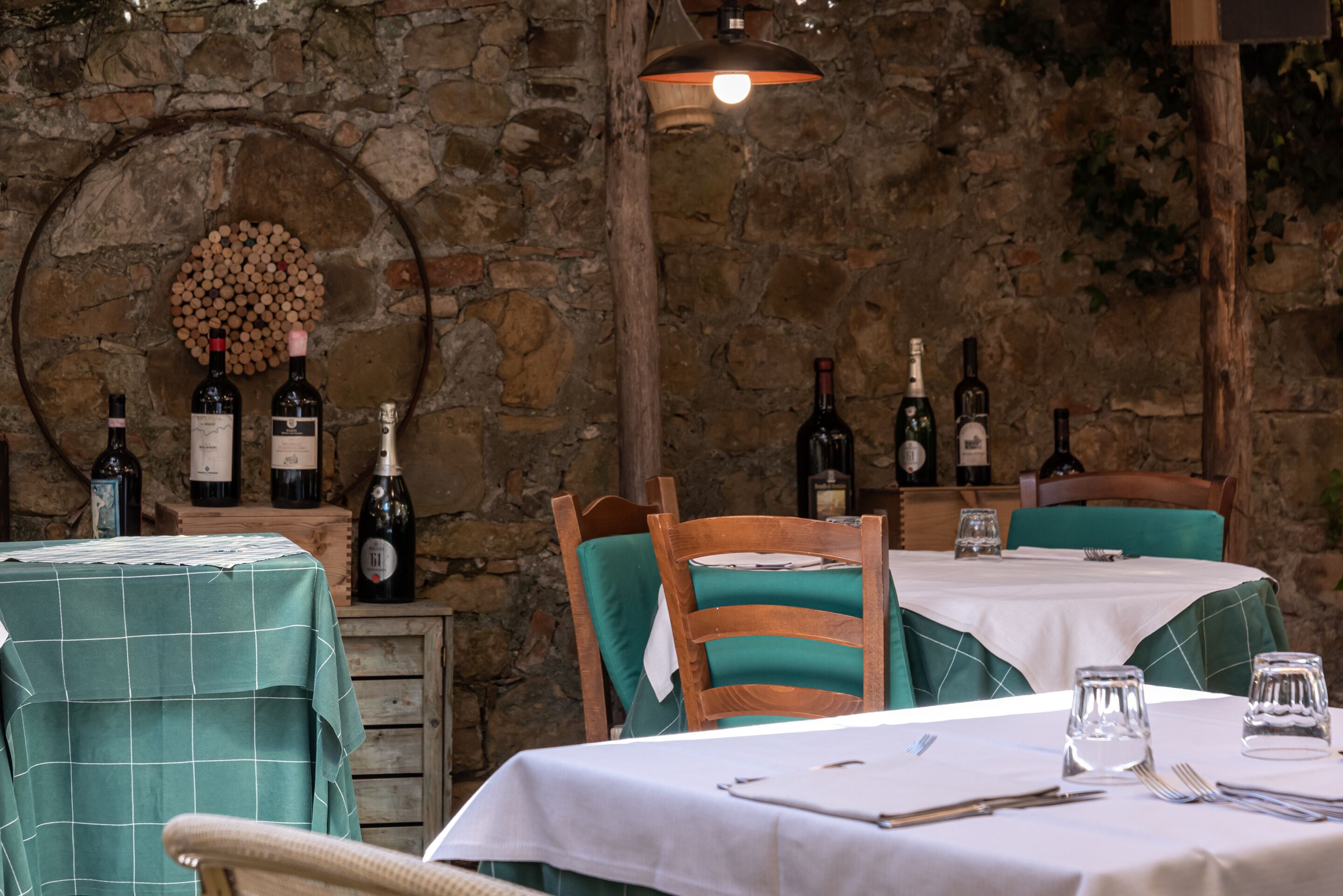 A rustic dining area with stone walls, wooden chairs, and tables set for two.