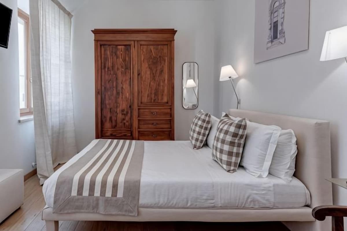 A bedroom with a bed, a wardrobe, a bedside table, and a lamp.