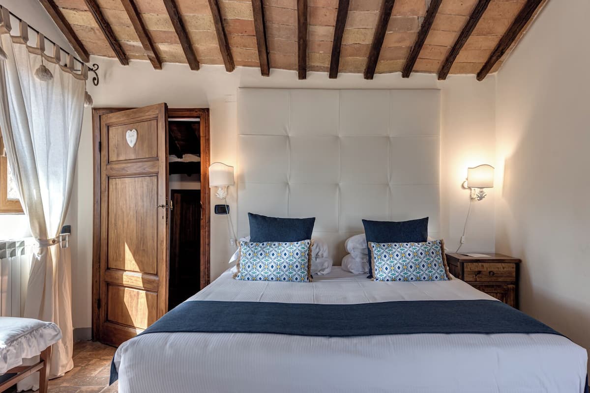 Een slaapkamer met een groot bed, houten balken in het plafond, een kledingkast en bedlampen.